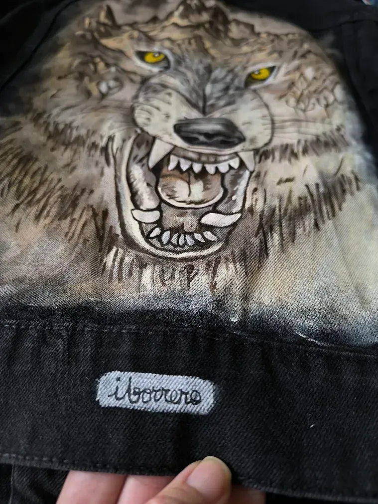 Una persona sostiene una chaqueta negra con una pintura de un lobo en ella.