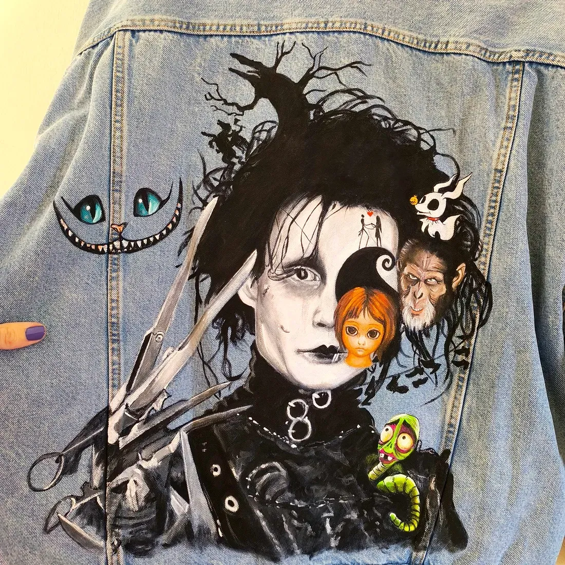 Una persona sostiene una chaqueta vaquera con una pintura de Eduardo Manostijeras.