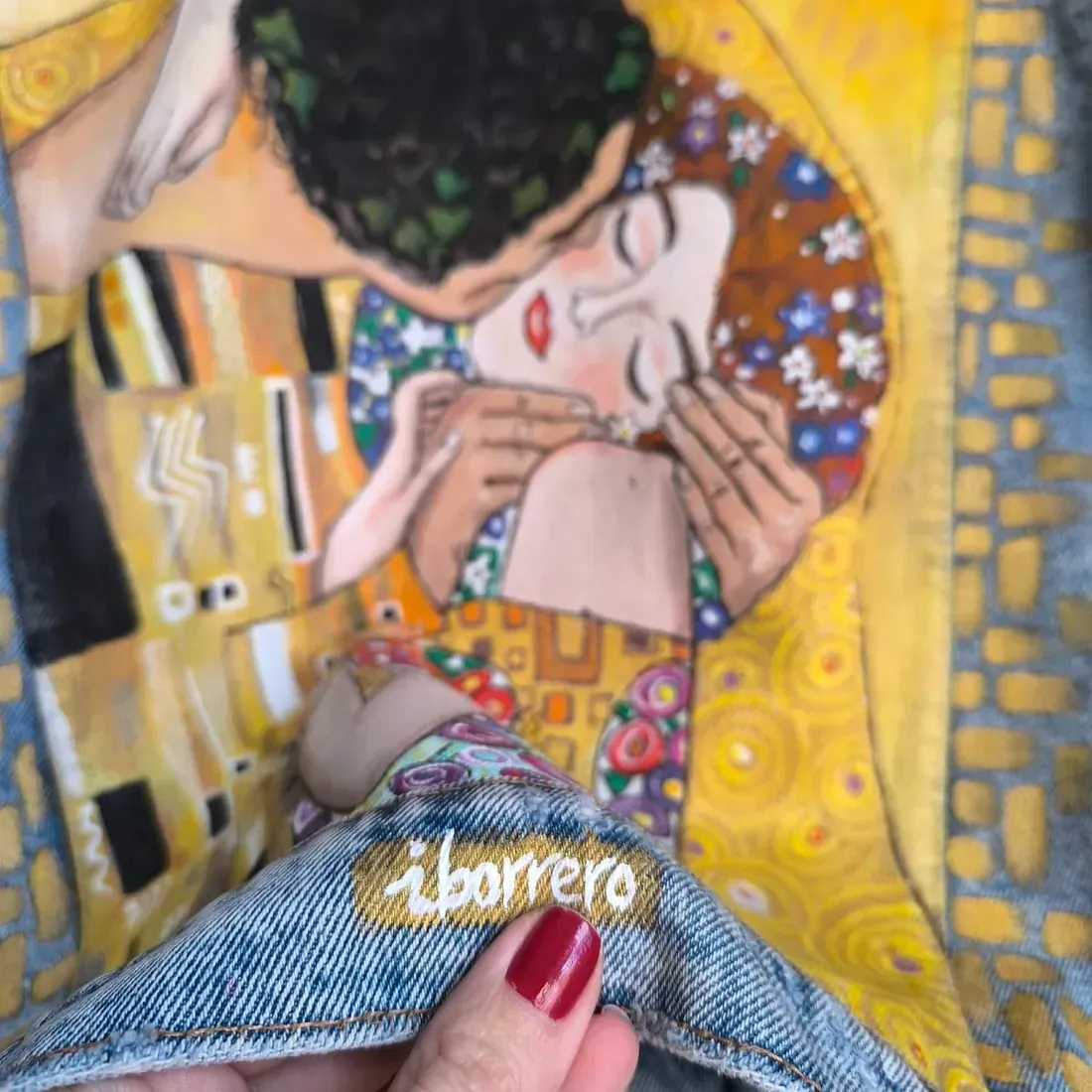 Una persona sostiene una chaqueta vaquera con una pintura de un hombre y una mujer besándose.