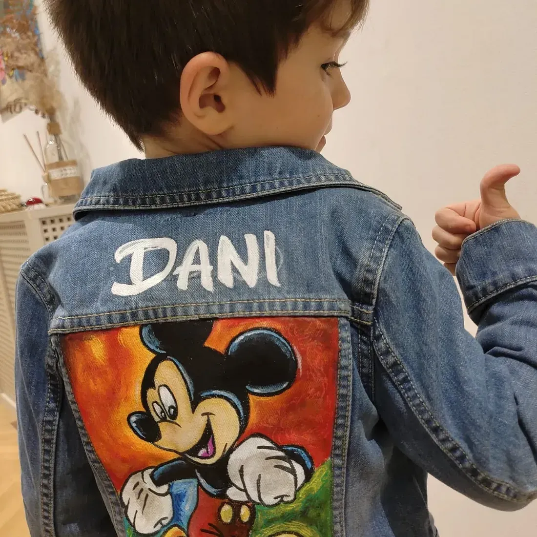 Un niño pequeño que lleva una chaqueta vaquera con Mickey Mouse pintado en la espalda.