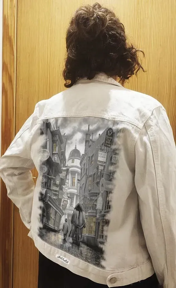 Una mujer lleva una chaqueta vaquera blanca con una pintura en la espalda.