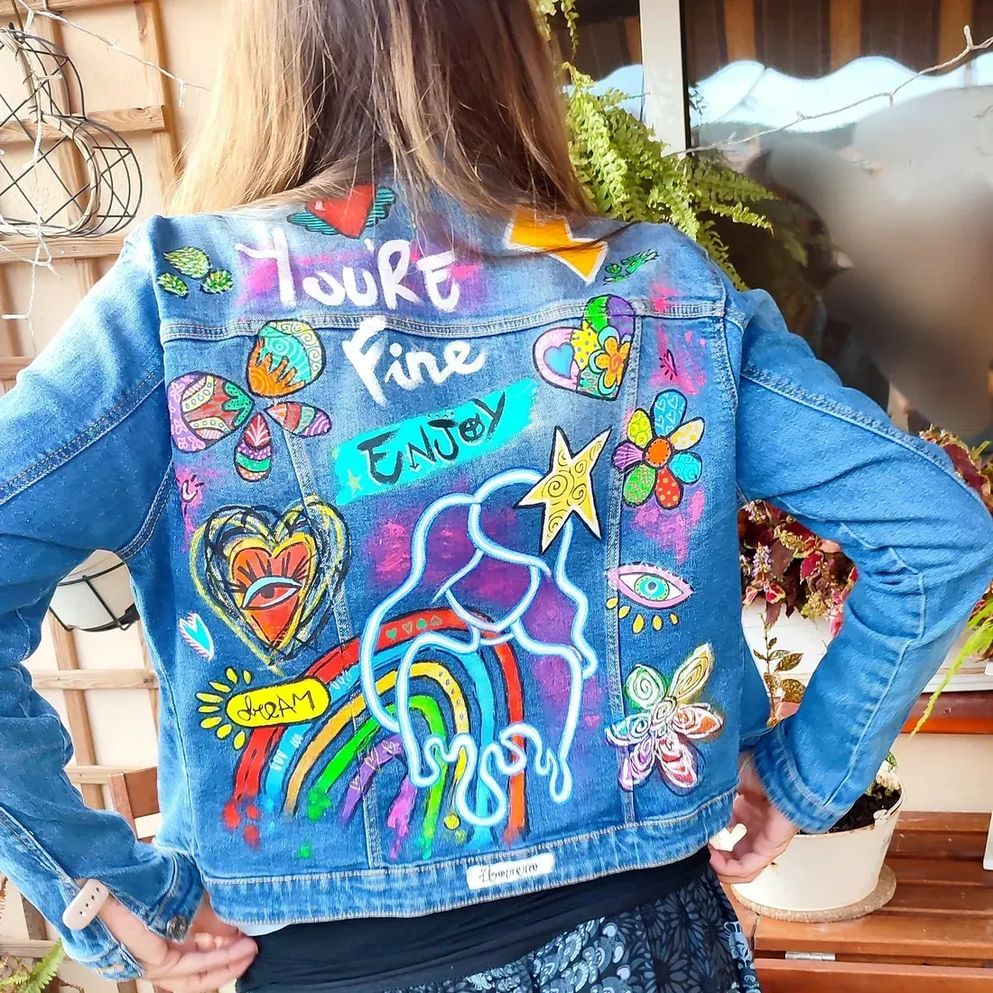 Una mujer lleva una chaqueta vaquera con un arcoíris y flores pintadas en ella.