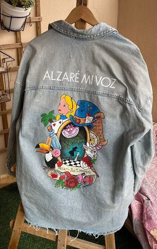 Una chaqueta vaquera con una pintura de Alicia en el país de las maravillas en la espalda está colgada en una percha.