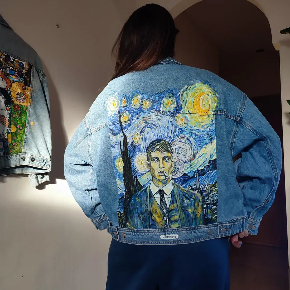 Una mujer que lleva una chaqueta vaquera con una pintura de una noche estrellada en la espalda.
