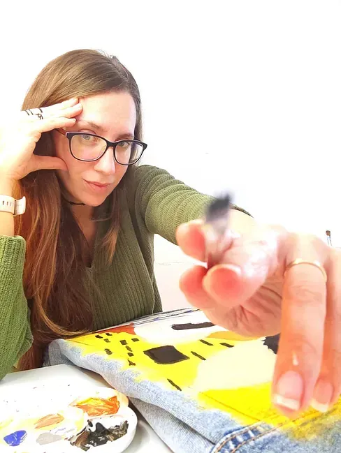 Una mujer con gafas está pintando un cuadro con un pincel.