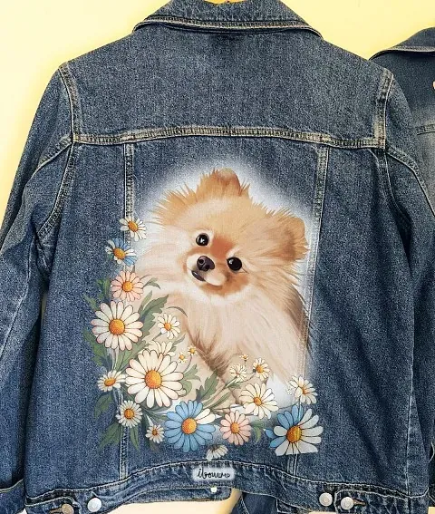 Una chaqueta vaquera con una pintura de un perro pomerania rodeado de margaritas.
