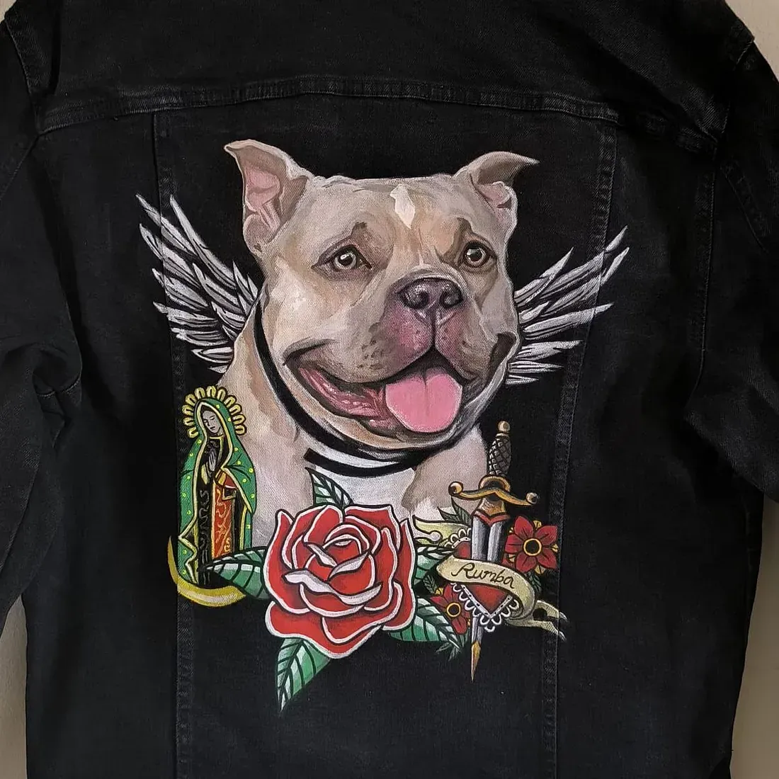Un cuadro de un perro con alas y una rosa en la espalda de una chaqueta vaquera negra.