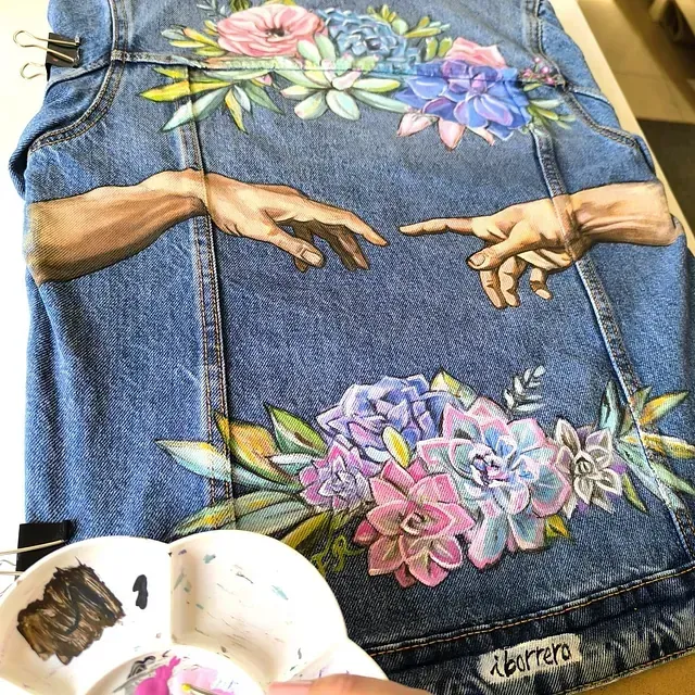 Una pintura de manos y flores en una chaqueta vaquera.
