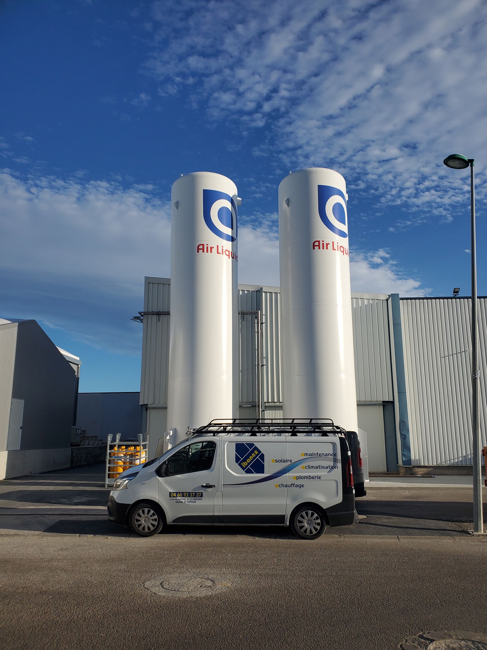 Une camionnette de service blanche garée à côté de grands silos industriels sous un ciel bleu
