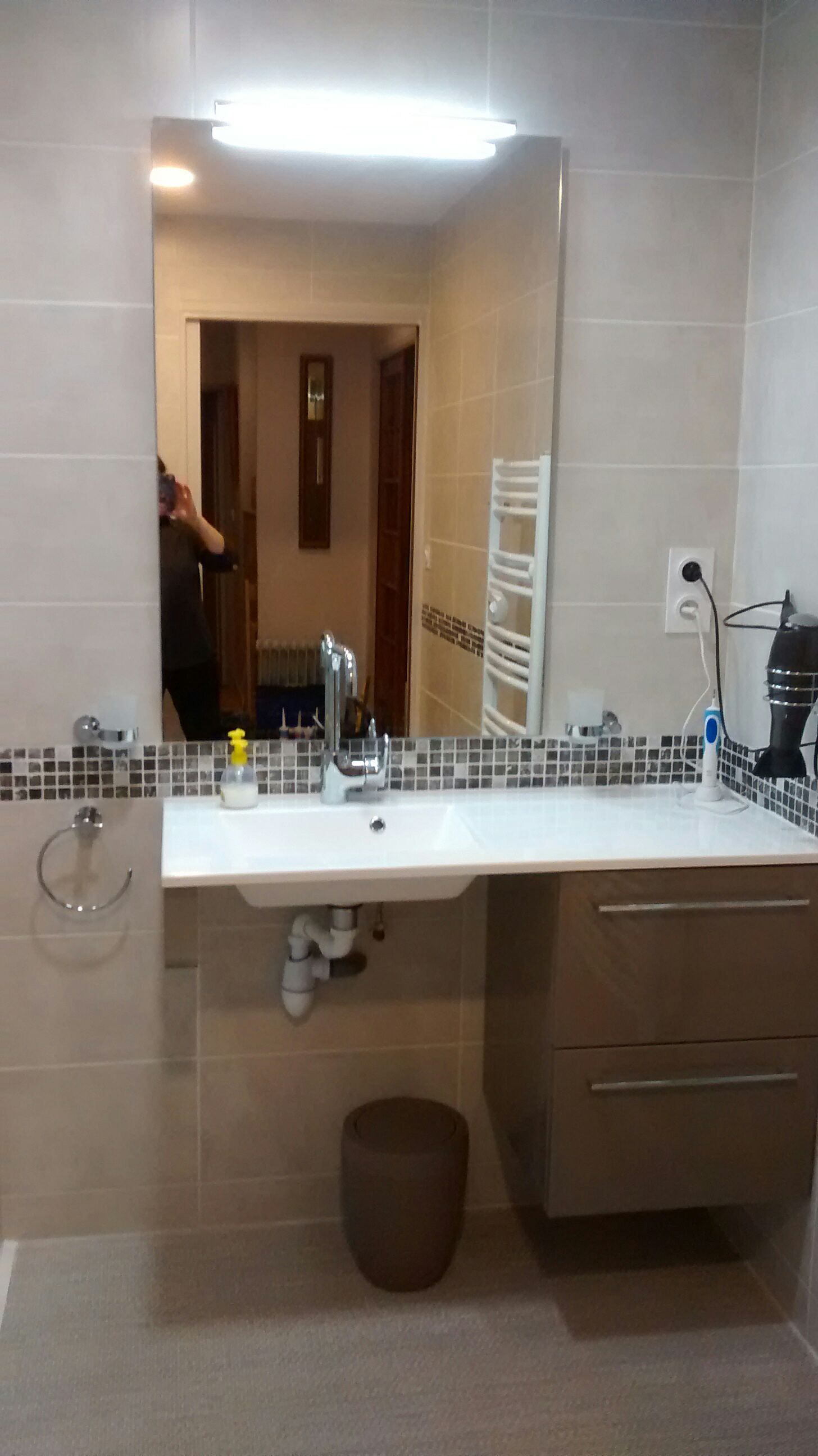 Salle de bains moderne avec grand miroir, lavabo blanc, murs carrelés beige et meuble-lavabo en bois