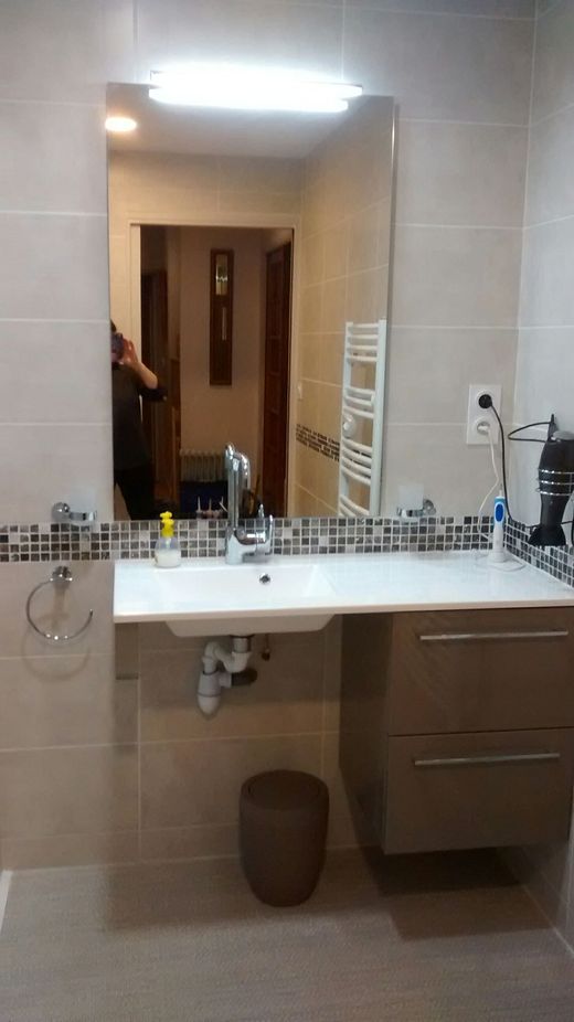 Salle de bains moderne avec grand miroir, lavabo blanc, murs carrelés beige et meuble-lavabo en bois