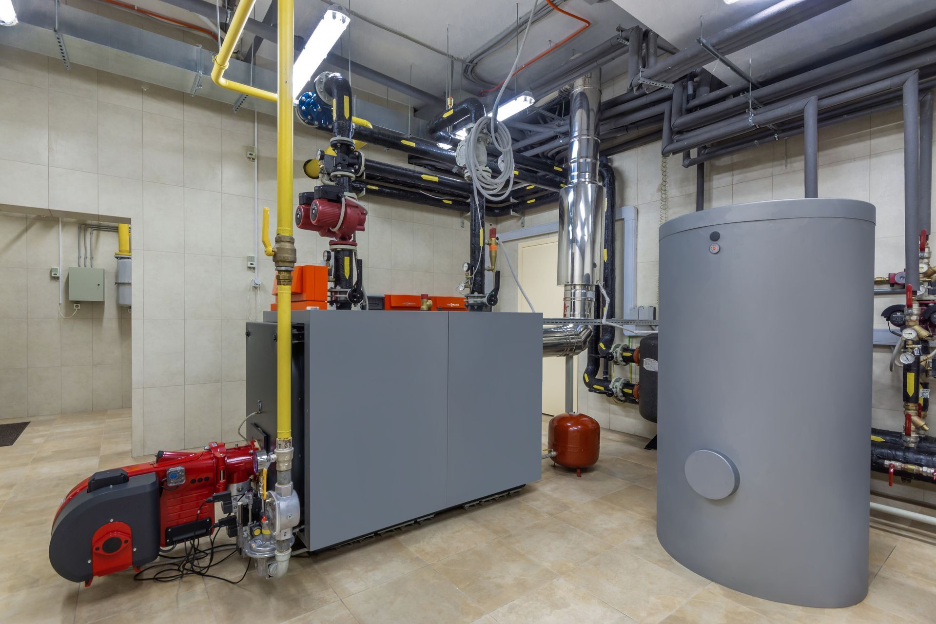Chaufferie industrielle avec des machines grises, des tuyaux rouges et un grand réservoir cylindrique