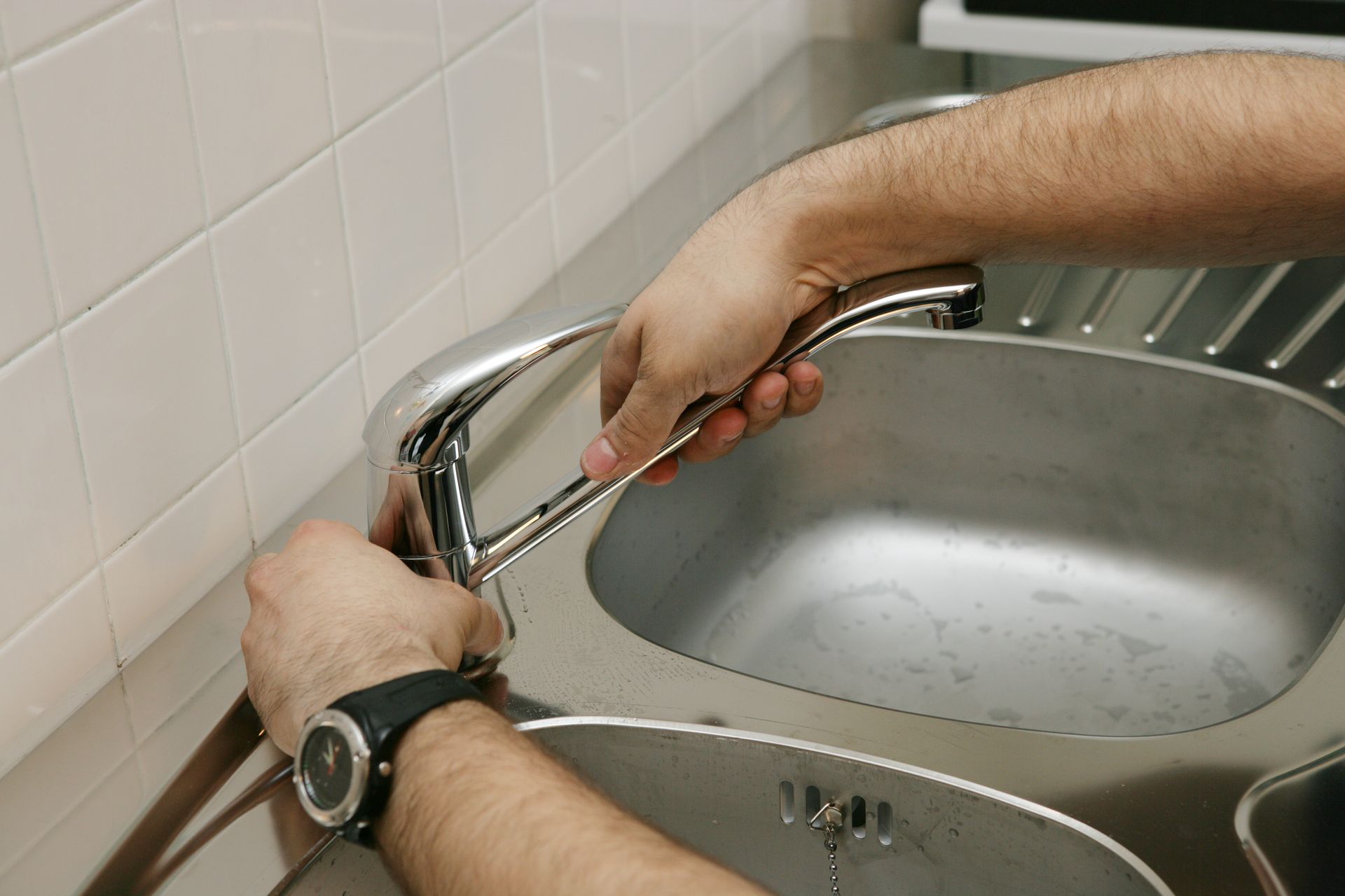 Des mains utilisent une clé pour réparer un robinet d'un évier en acier inoxydable.