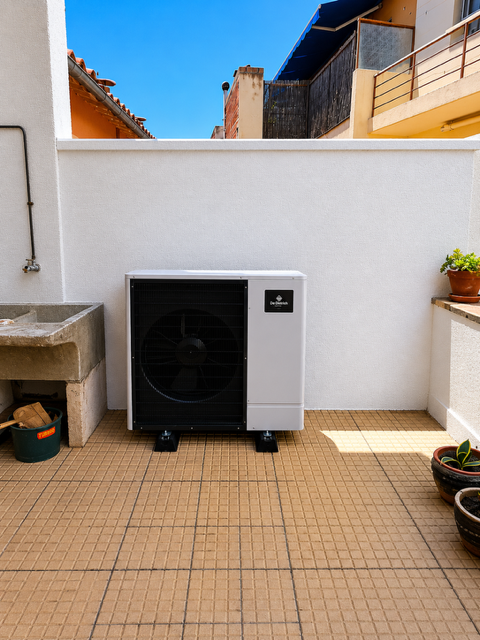 Unité de climatisation extérieure sur une terrasse carrelée à côté d'un mur blanc, avec des plantes en pot et un évier à proximité.