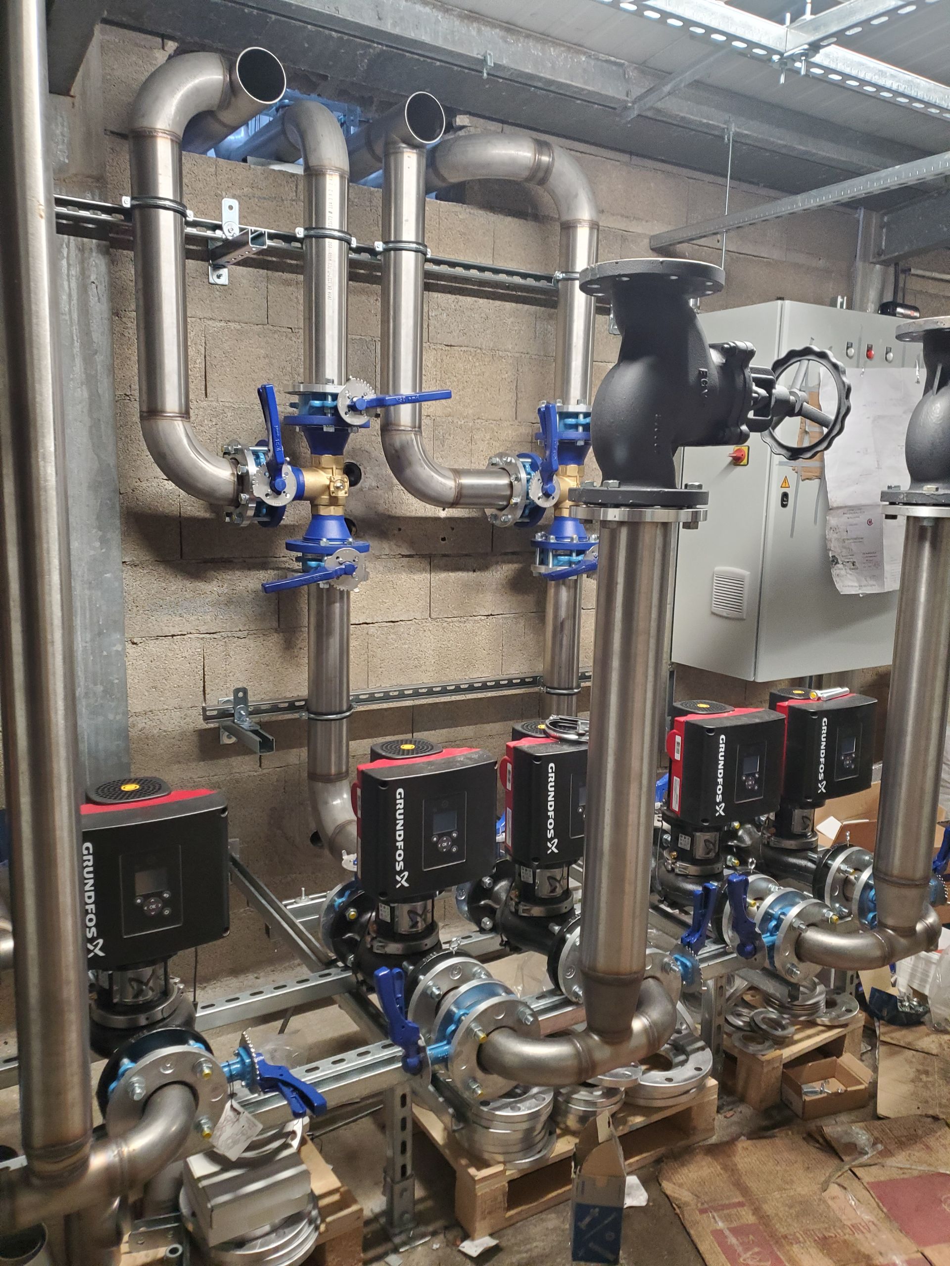 Ensemble de pompe et de tuyauterie industrielle avec vannes bleues et groupes motopropulseurs noirs dans une salle des machines.