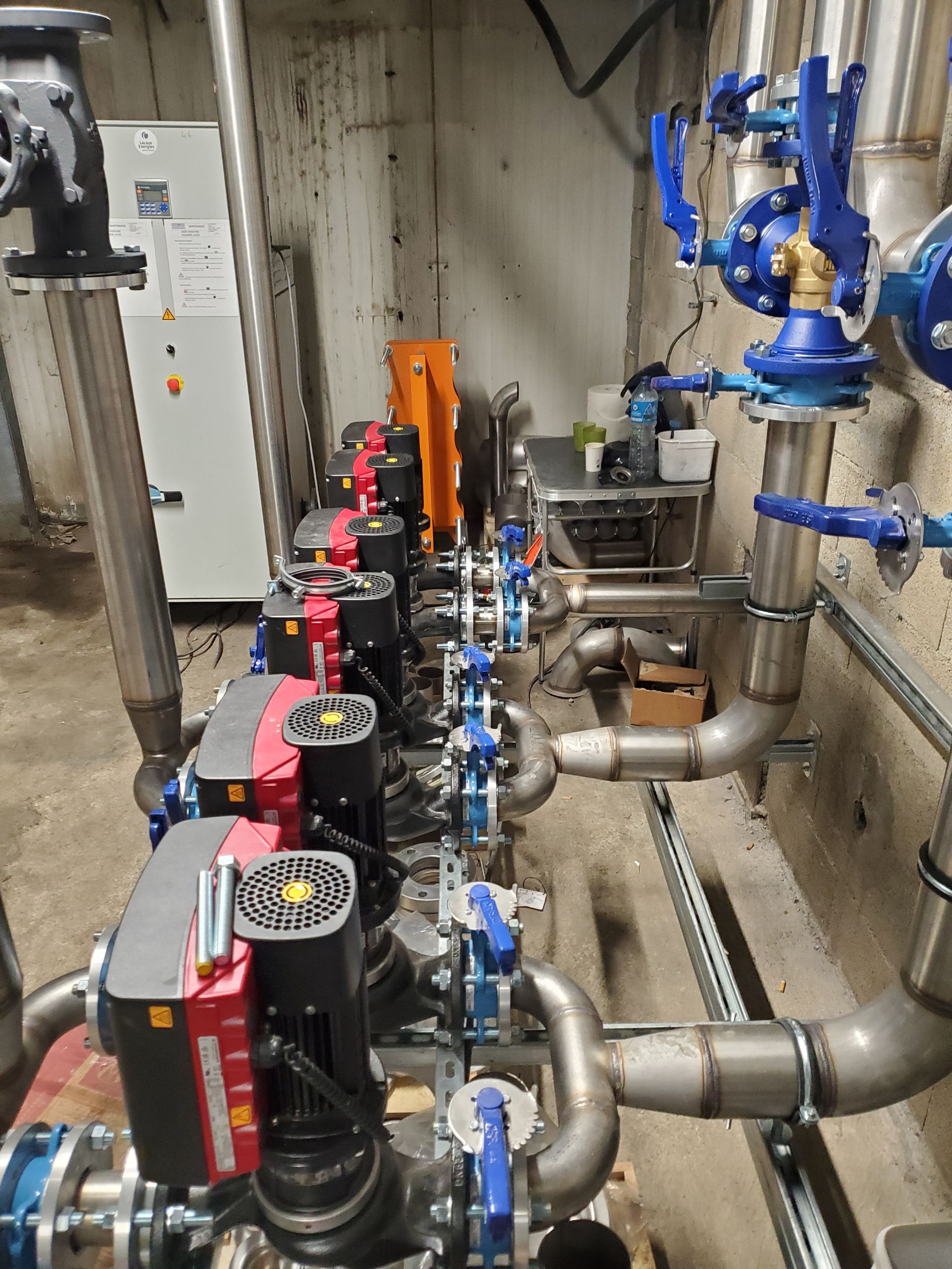 Système de pompes et de tuyauteries industrielles avec vannes bleues et moteurs rouges dans une salle technique
