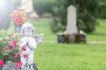 Ein Engel in Gebetshaltung mit Blumen auf einem Friedhof