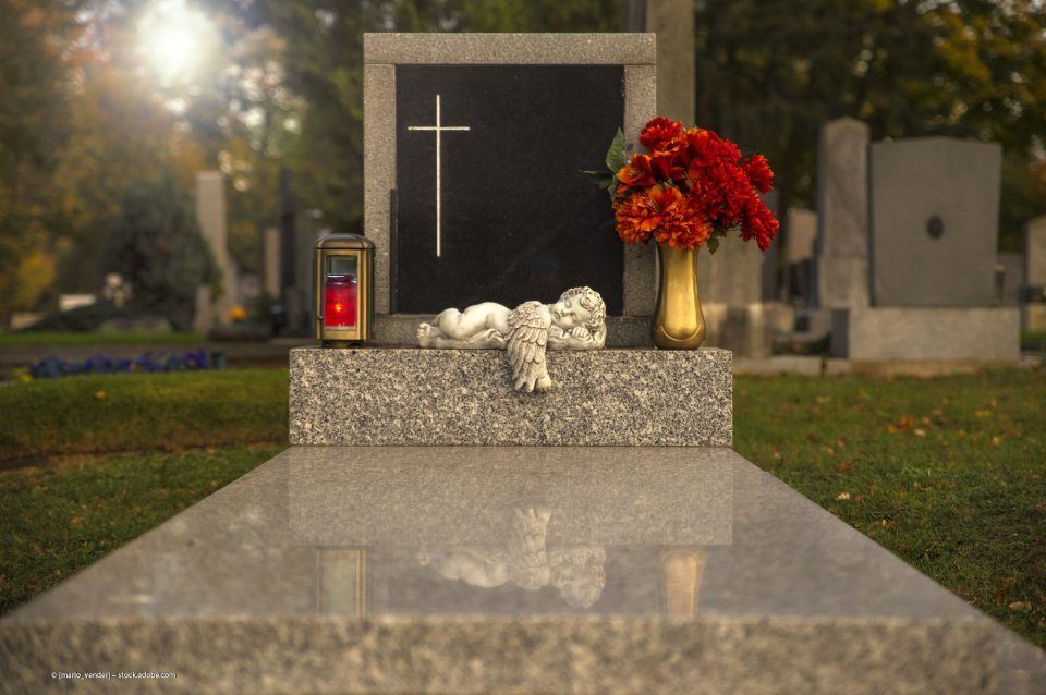 Engel-Statue liegt auf einem Grab mit Rosen