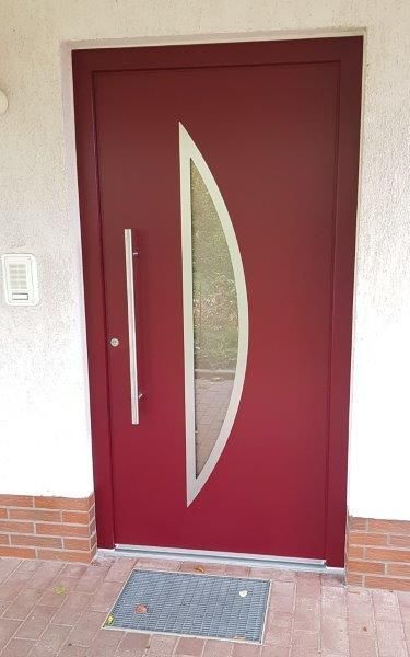 Eine rote Tür mit einem Edelstahlgriff und einem halbmondförmigen Fenster
