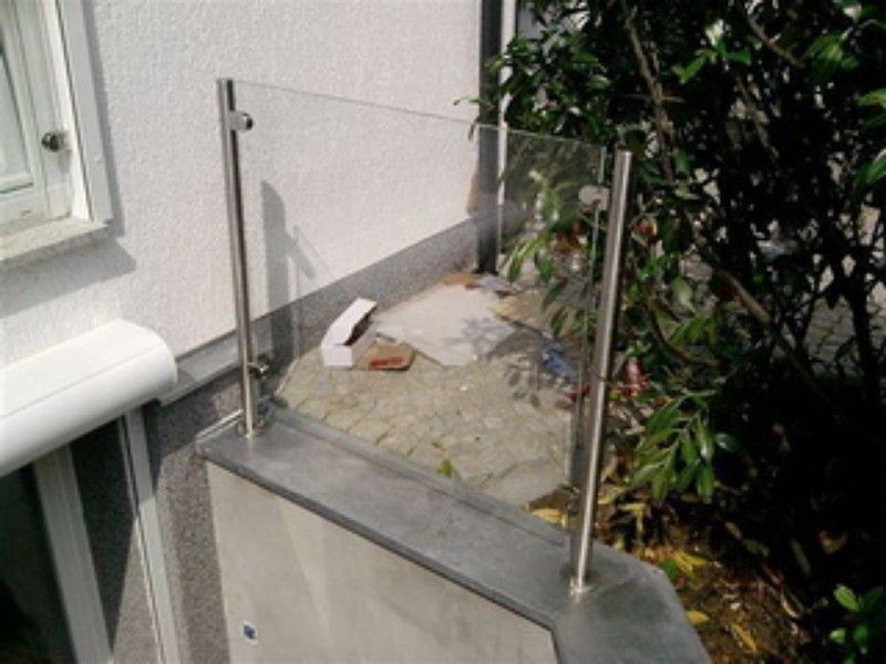 An der Seite eines Gebäudes ist ein Edelstahlgeländer mit einer klaren Glasplatte angebracht.