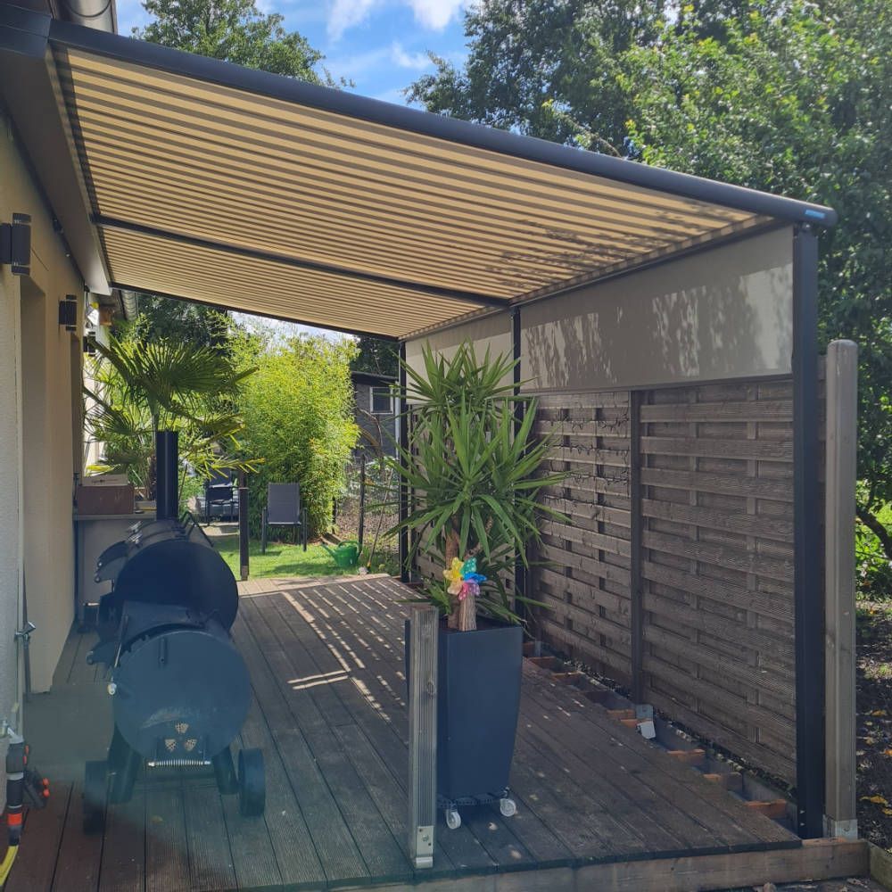 Eine Holzterrasse mit Kinderwagen und Grill unter einem Vordach.