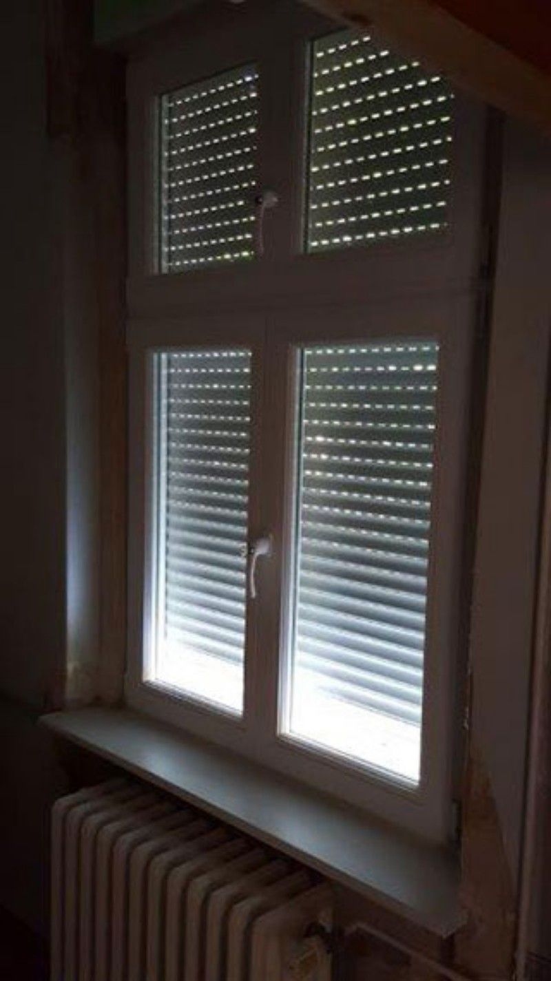 Ein Fenster mit Rollläden und einem Heizkörper in einem dunklen Raum.