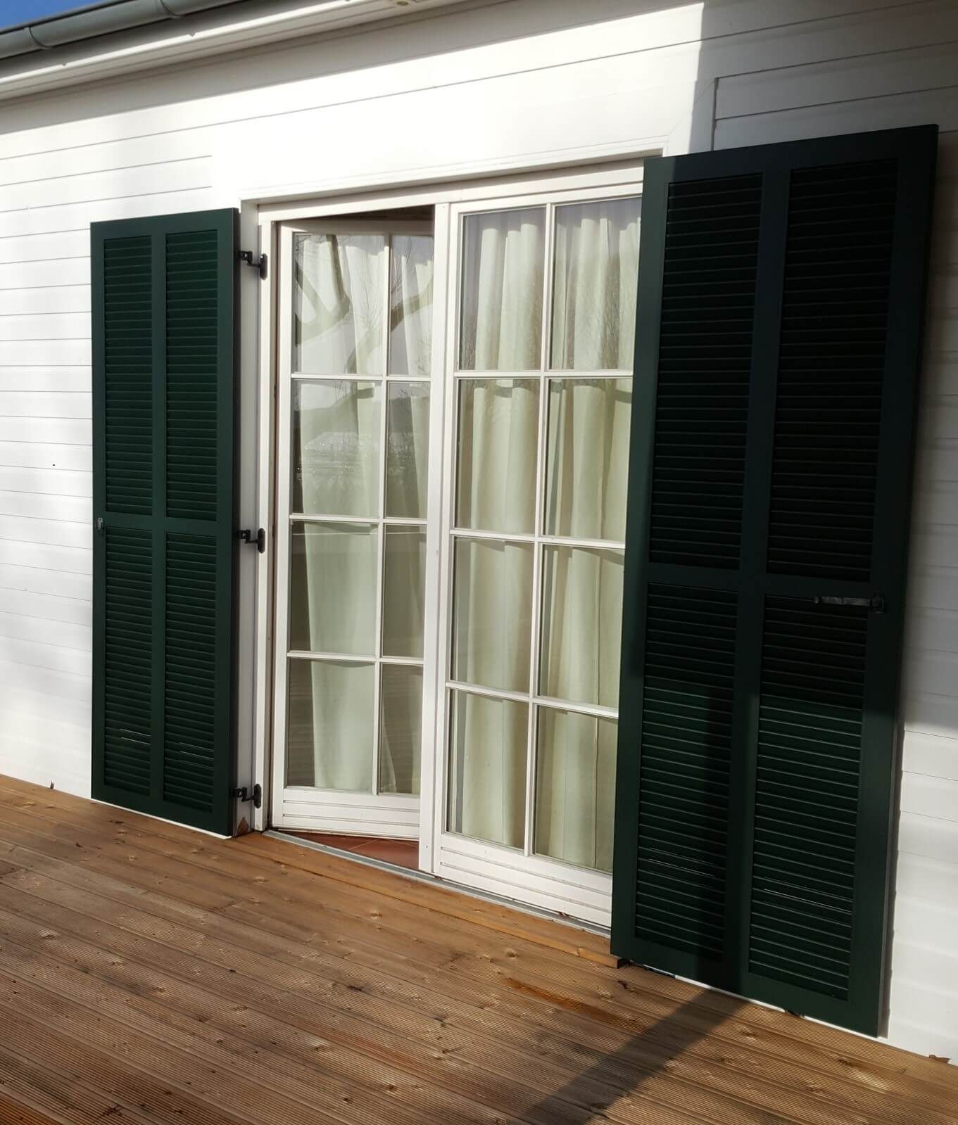 Ein weißes Haus mit grünen Fensterläden und einer Glasschiebetür