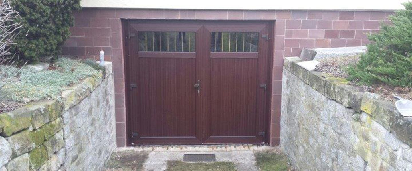 Neben einer Steinmauer steht ein hölzernes Garagentor.