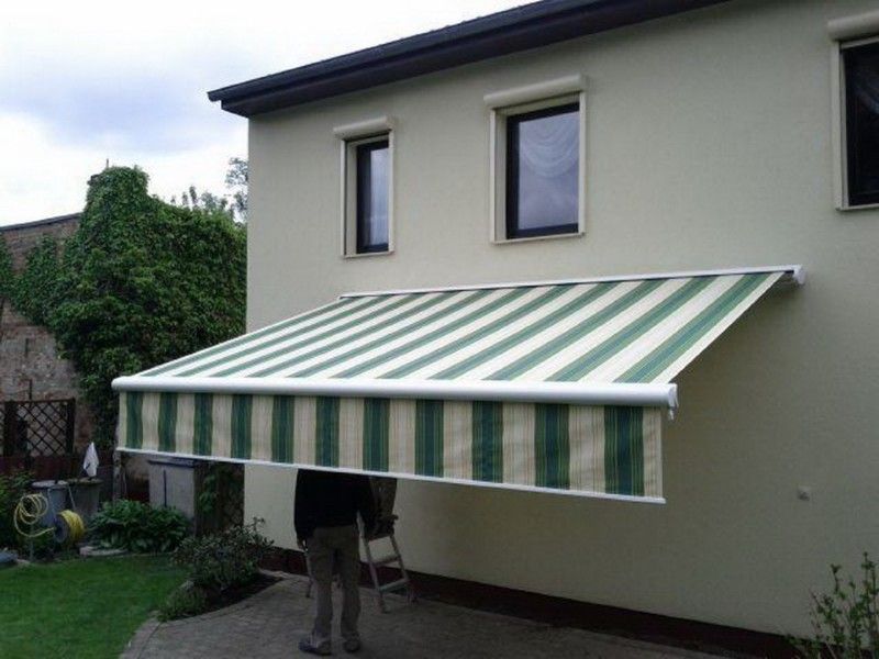 Ein Mann steht unter einer grün-weiß gestreiften Markise an der Seite eines Hauses.