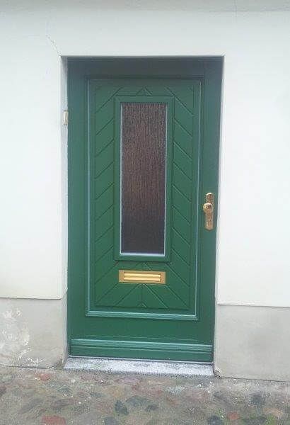 An der Seite eines Gebäudes befindet sich eine grüne Tür mit einem Glasfenster.