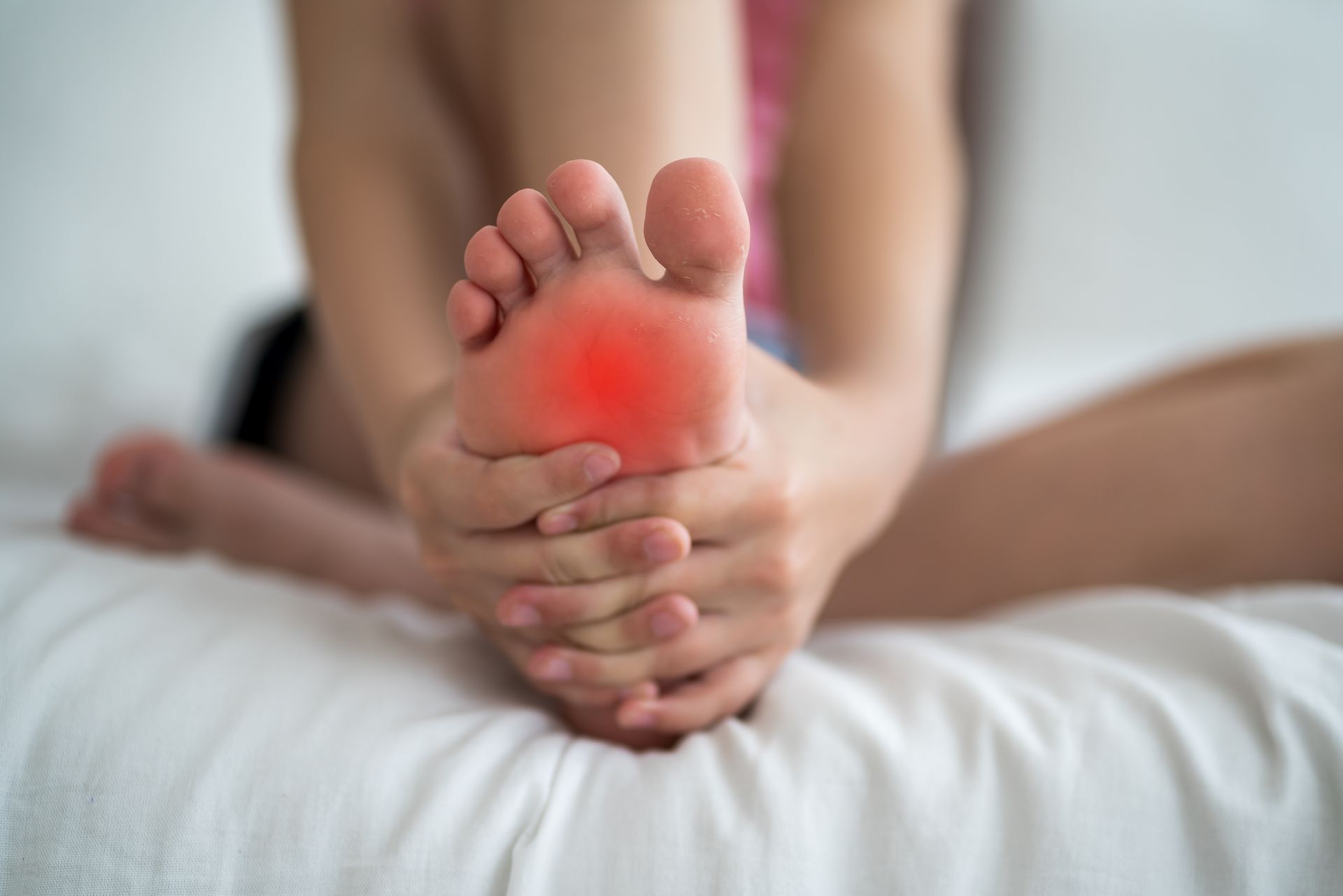 Une femme est assise sur un lit et se tient le pied de douleur.