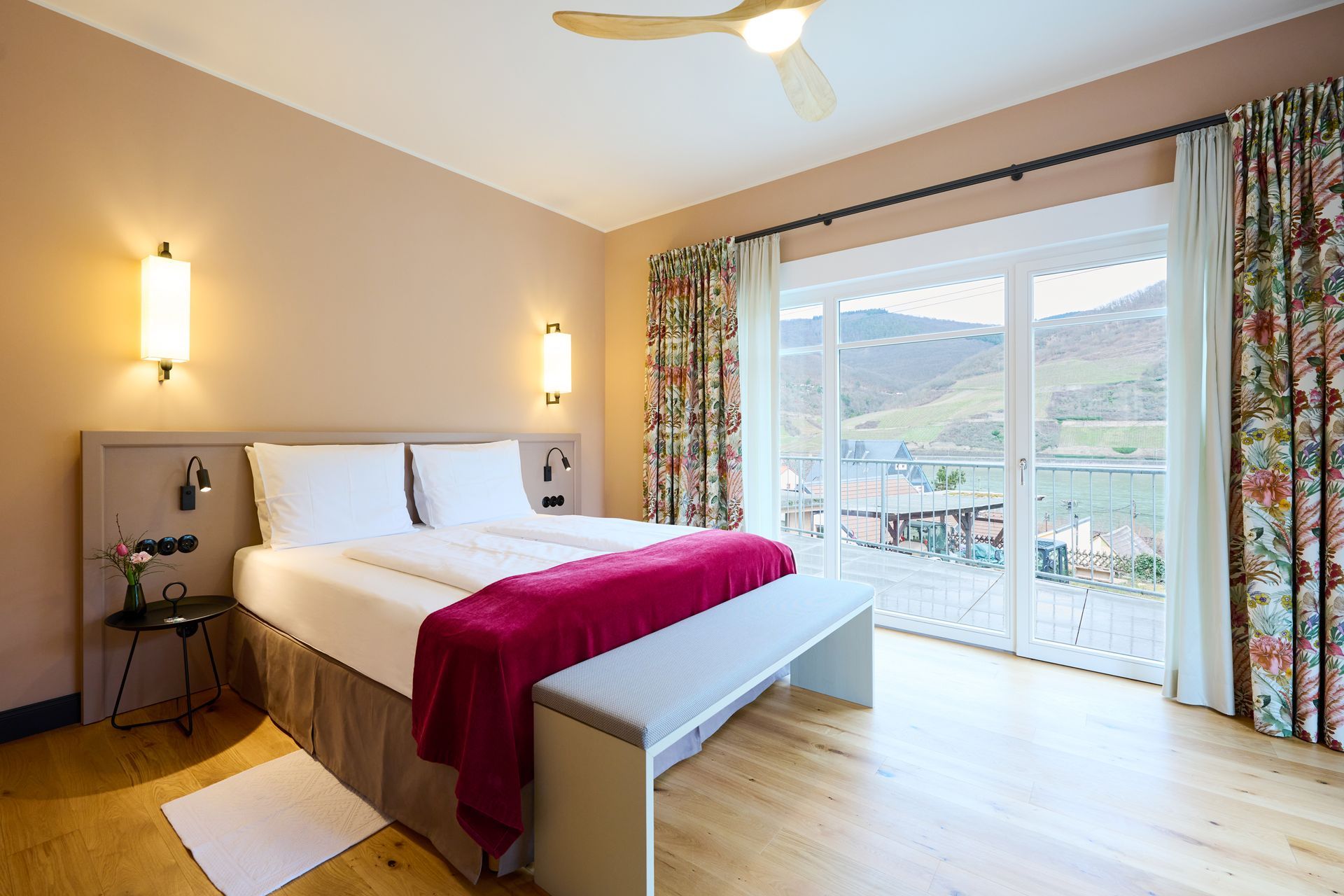 Ein Hotelzimmer mit Queensize-Bett, magentafarbener Tagesdecke, Holzboden und Balkon mit Bergblick.