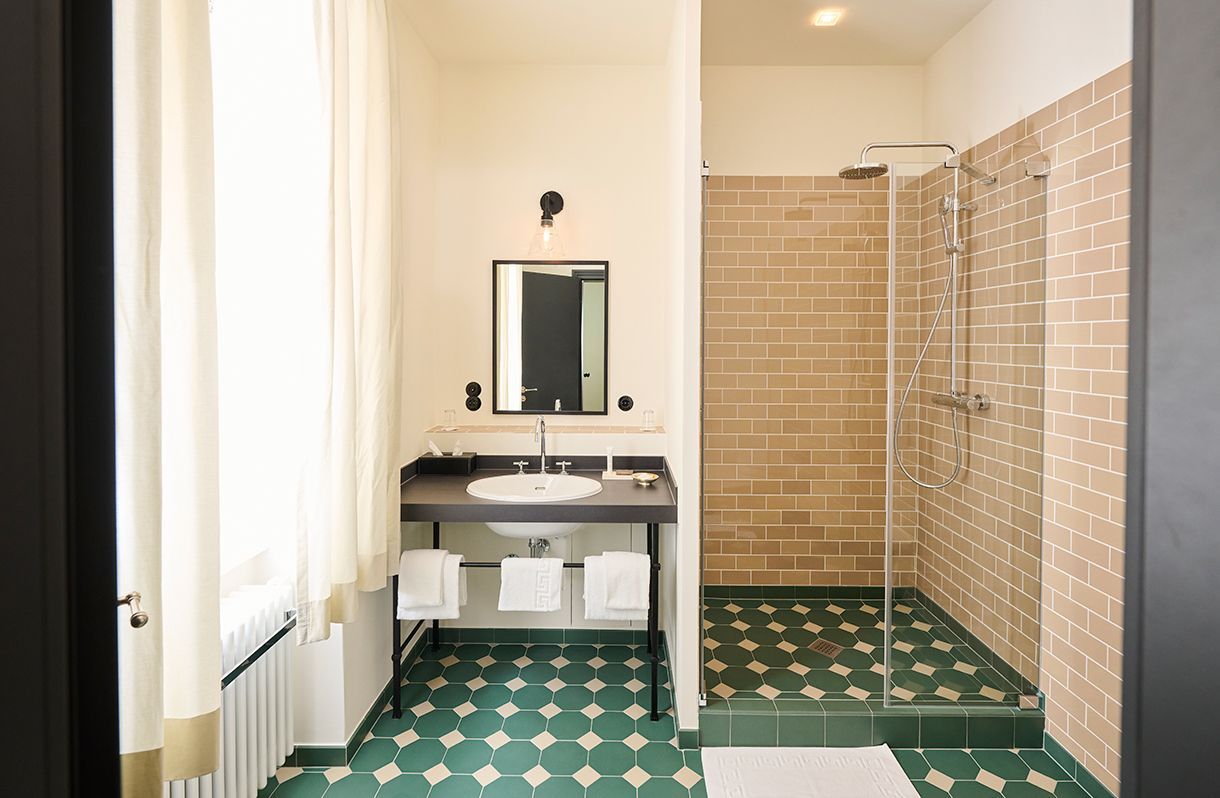 Ein modernes Badezimmer mit schwarzem Waschtisch, quadratischem Spiegel, grünen Fliesenböden und einer begehbaren Dusche mit hellbraunen Ziegelwänden.