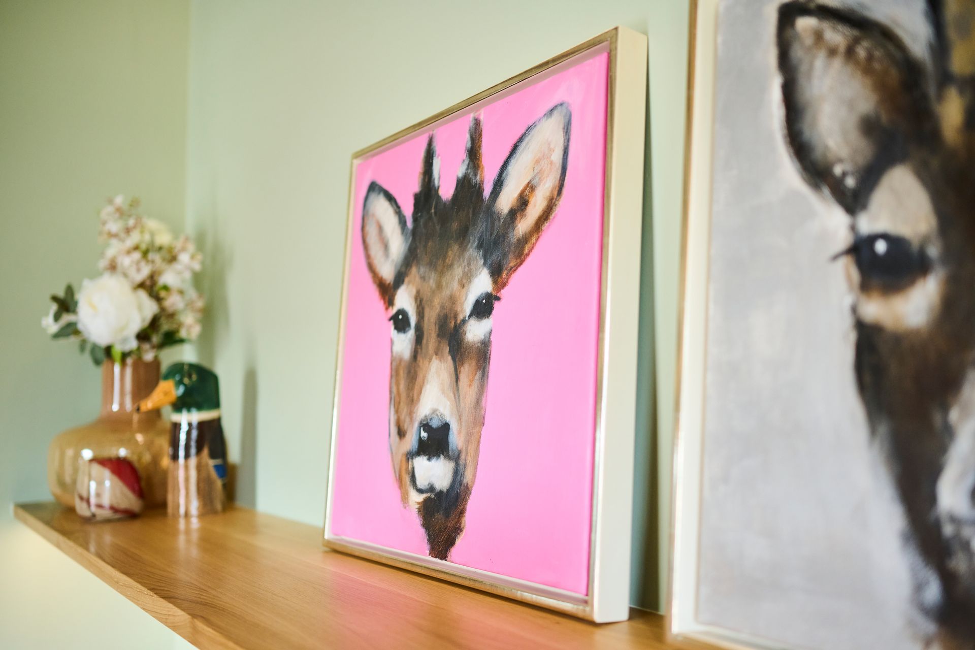 Zwei gerahmte Hirschporträts auf einem Holzregal neben einer Blumenvase und einer kleinen Deko-Ente.