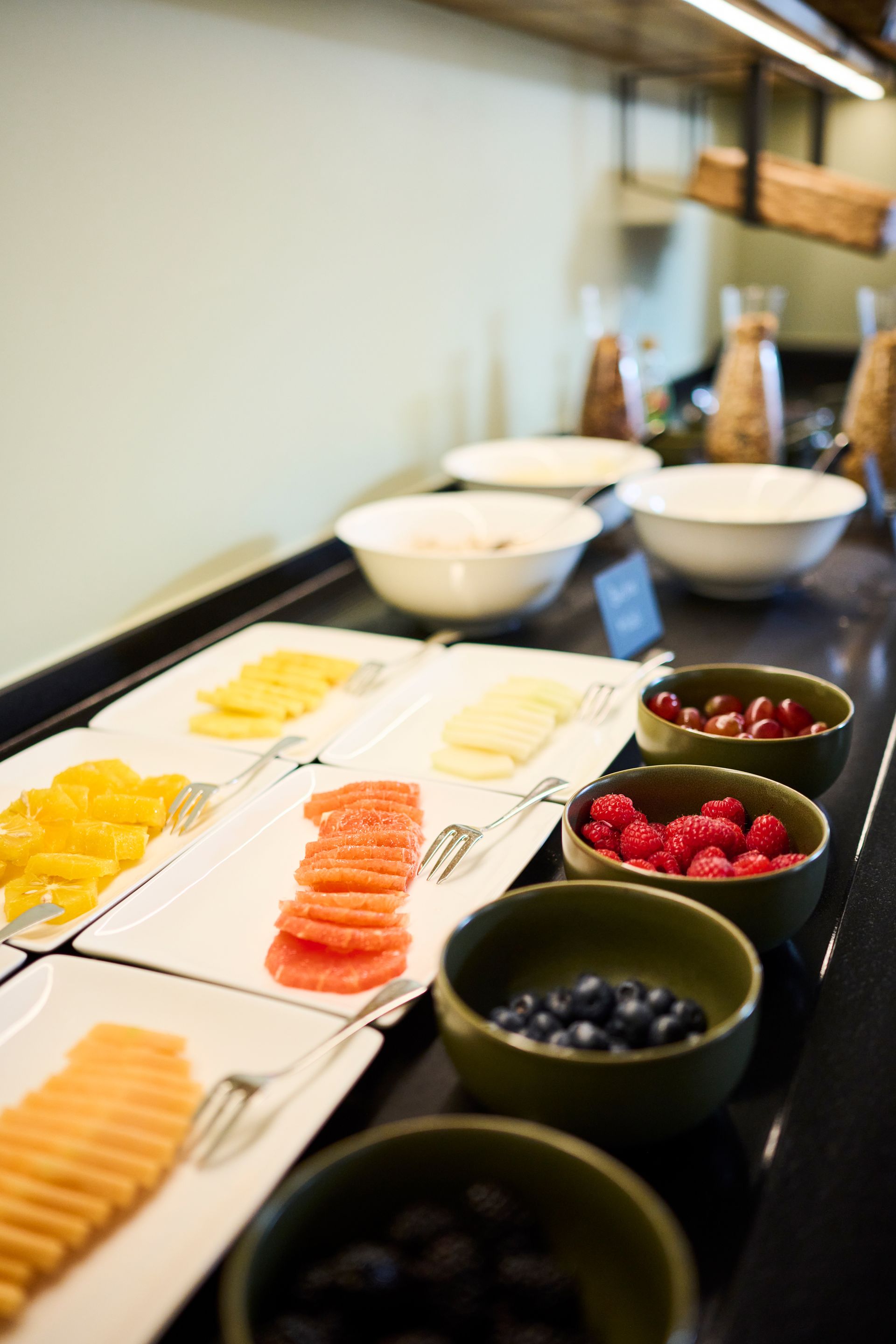 Ein Frühstücksbuffet mit durchsichtigen Karaffen mit Müsli und Schüsseln mit verschiedenen Nüssen, Samen und Joghurt auf einer dunklen Oberfläche.