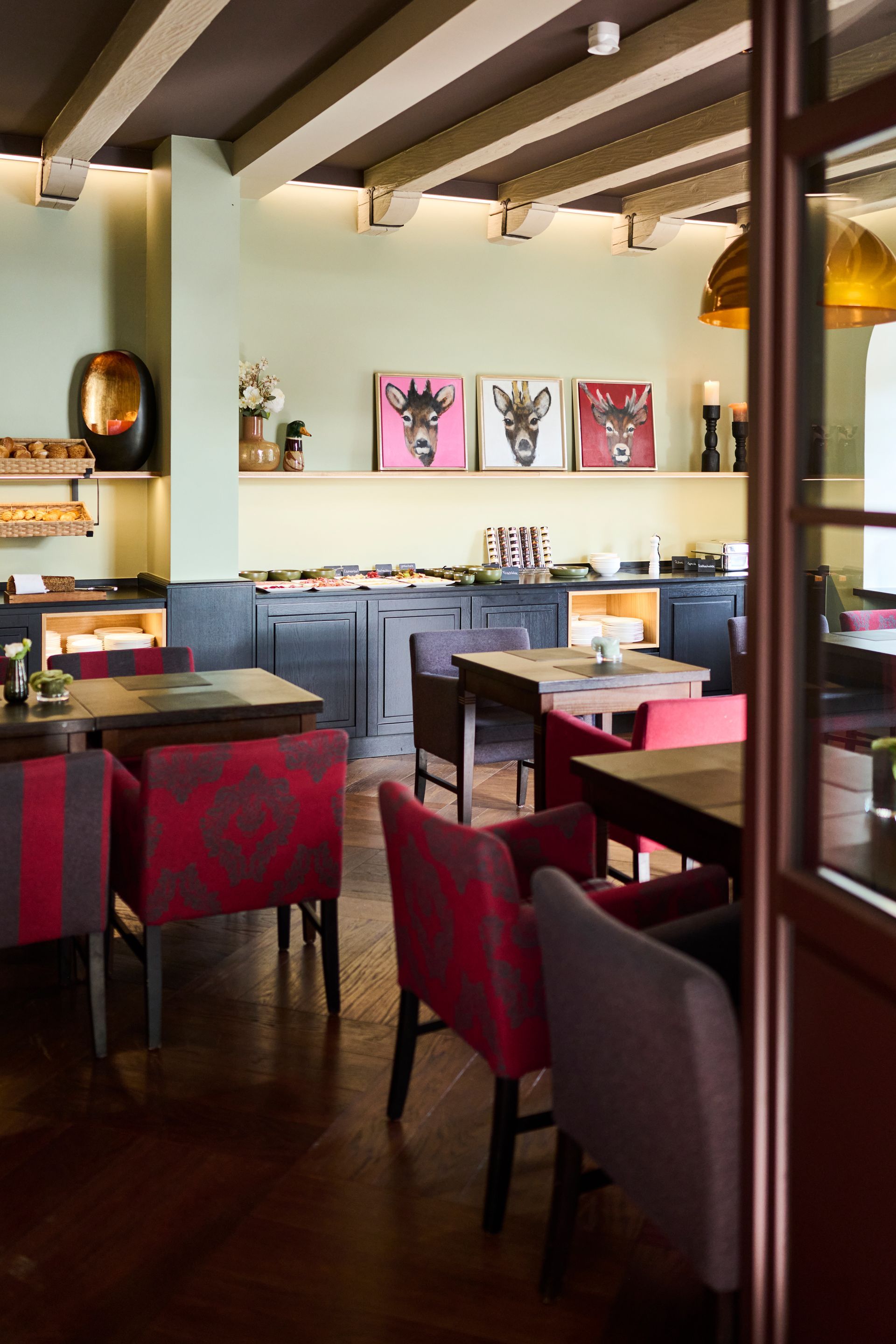 Ein Restaurantinterieur mit Holztischen und -stühlen mit rot gemusterten Bezügen und Tierporträts an der Wand.