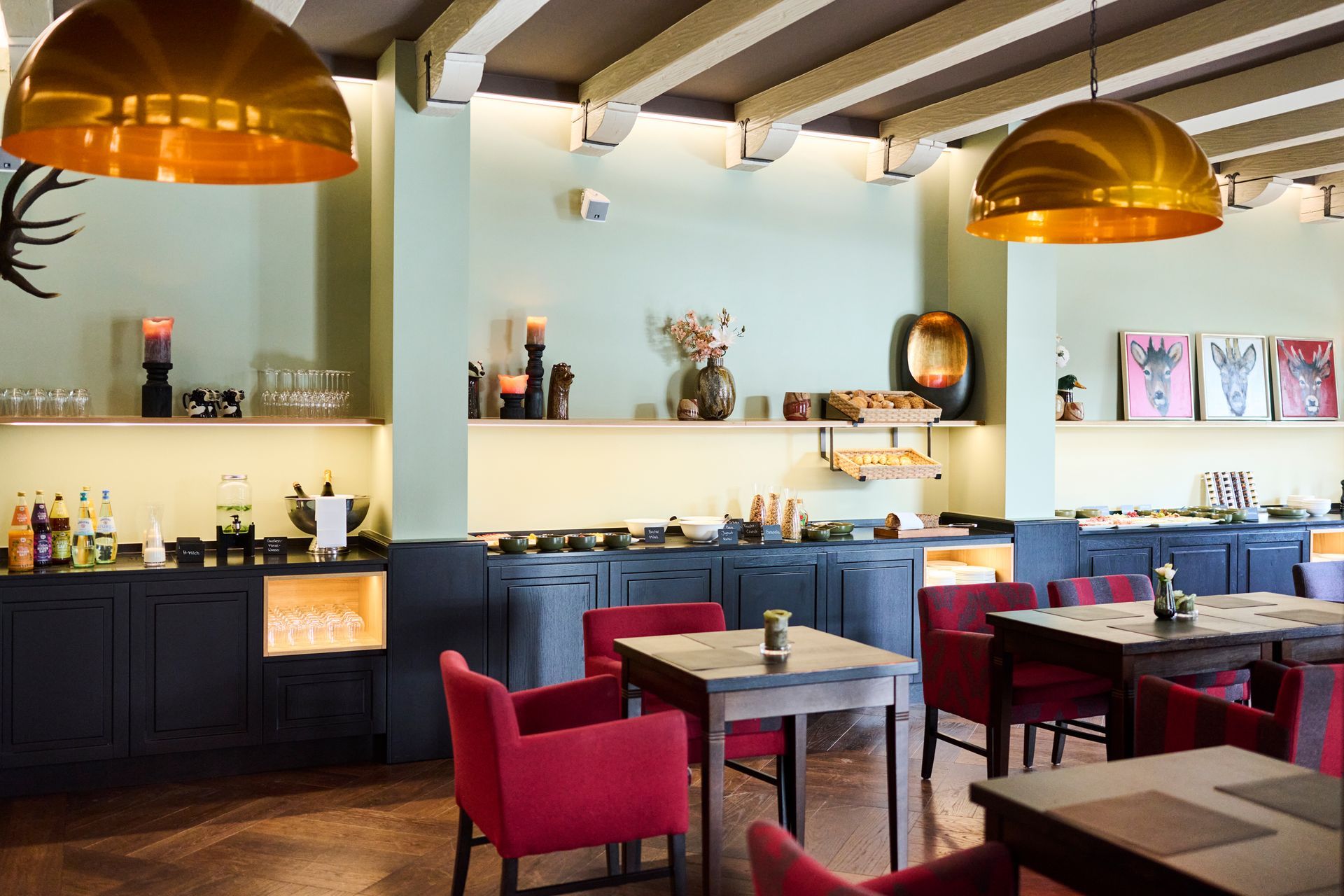 Ein Esszimmer mit dunkelblauen Schränken, einem Buffetbereich, Tischen mit roten Sesseln und zwei großen Messingkuppelleuchten.