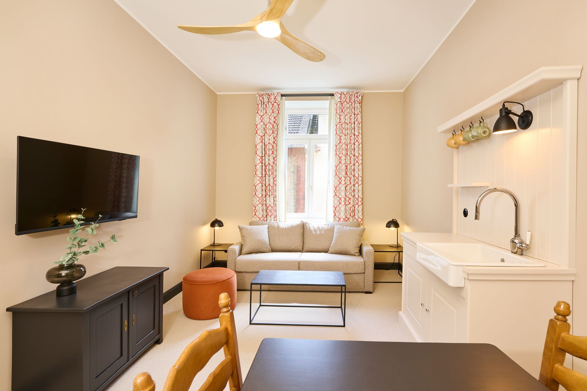 Ein gemütliches Studio-Apartment mit Wohnbereich, ausgestattet mit Sofa, Fernseher, Couchtisch und einer kleinen Küchenzeile mit Spüle.