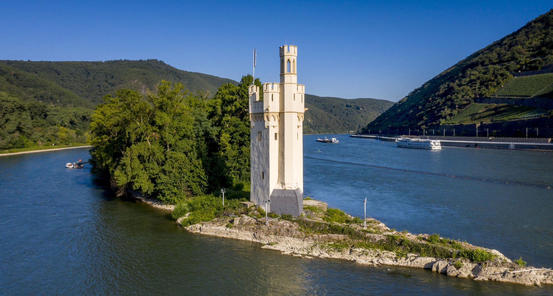 Der Mäuseturm steht auf einer Felseninsel mitten im Rhein, umgeben von üppigen, bewaldeten Hügeln.