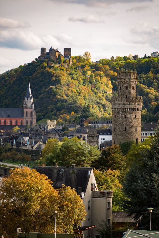 Im Vordergrund einer Stadt mit einer historischen Kirche und einer Burg auf einem bewaldeten Hügel erhebt sich ein Steinturm.