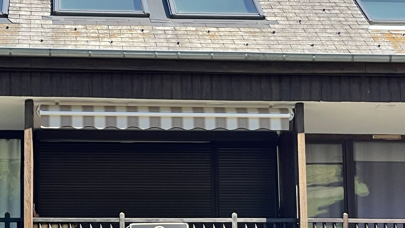 Store rayé au-dessus d'un balcon sous un toit à lucarne et des puits de lumière.
