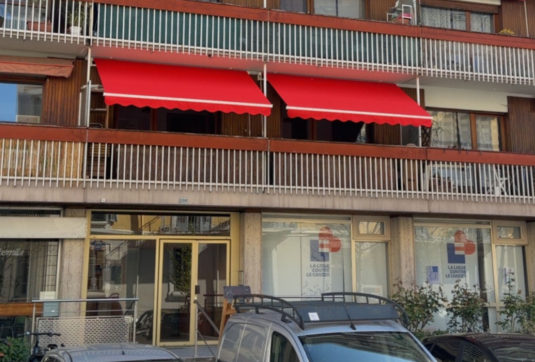 Façade d'appartement avec auvents rouge vif et véhicules stationnés dans une rue.