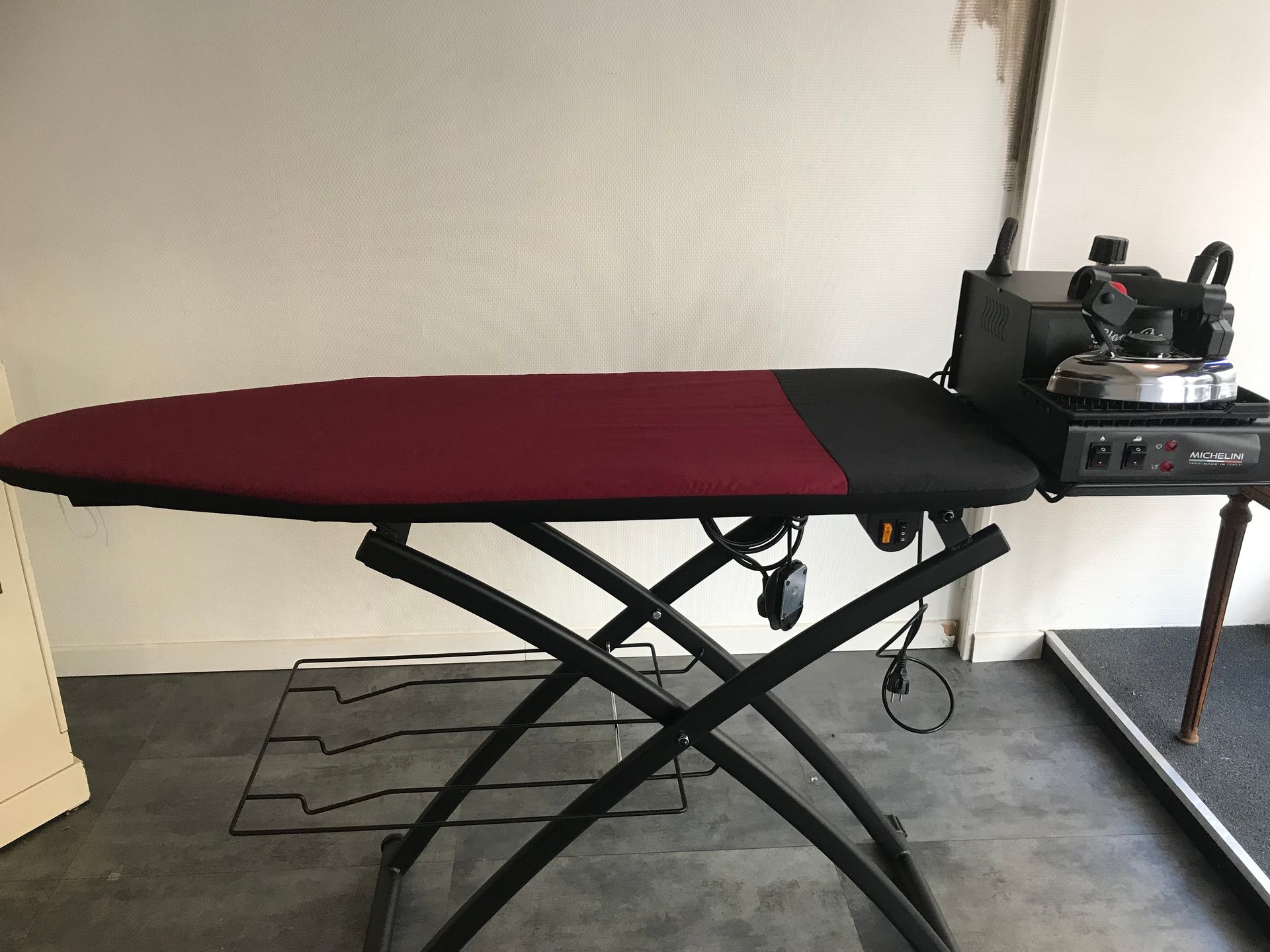 Un poste de repassage comprenant une table à repasser bordeaux et noire avec un fer à repasser à générateur de vapeur installé sur le côté.