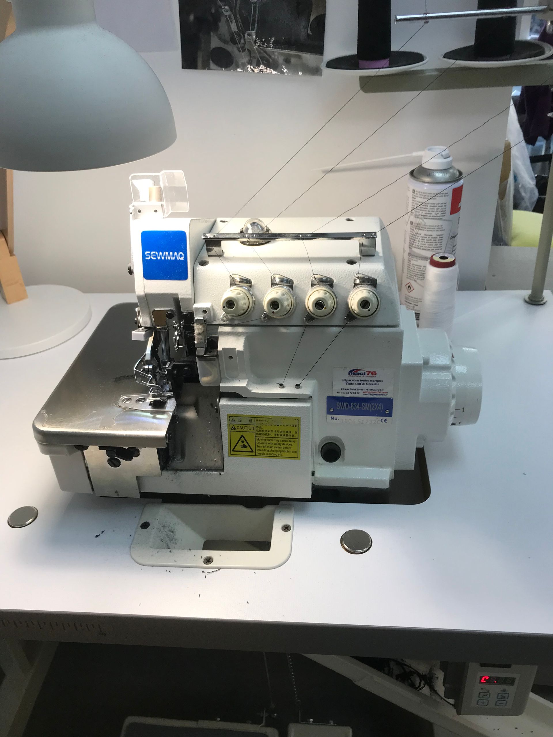 Une surjeteuse industrielle blanche est posée sur une table de travail blanche immaculée, sous une lampe.