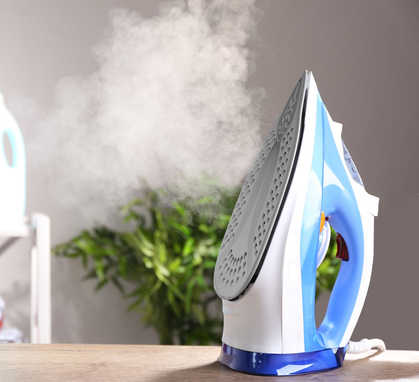 Un fer à repasser à vapeur bleu et blanc posé sur une surface en bois, libérant un épais nuage de vapeur dans l'air.