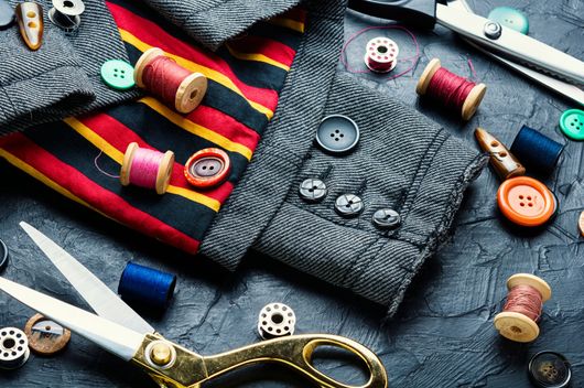 Fournitures de couture, notamment des bobines de fil, des boutons colorés et des ciseaux, disposées sur une surface sombre et texturée.