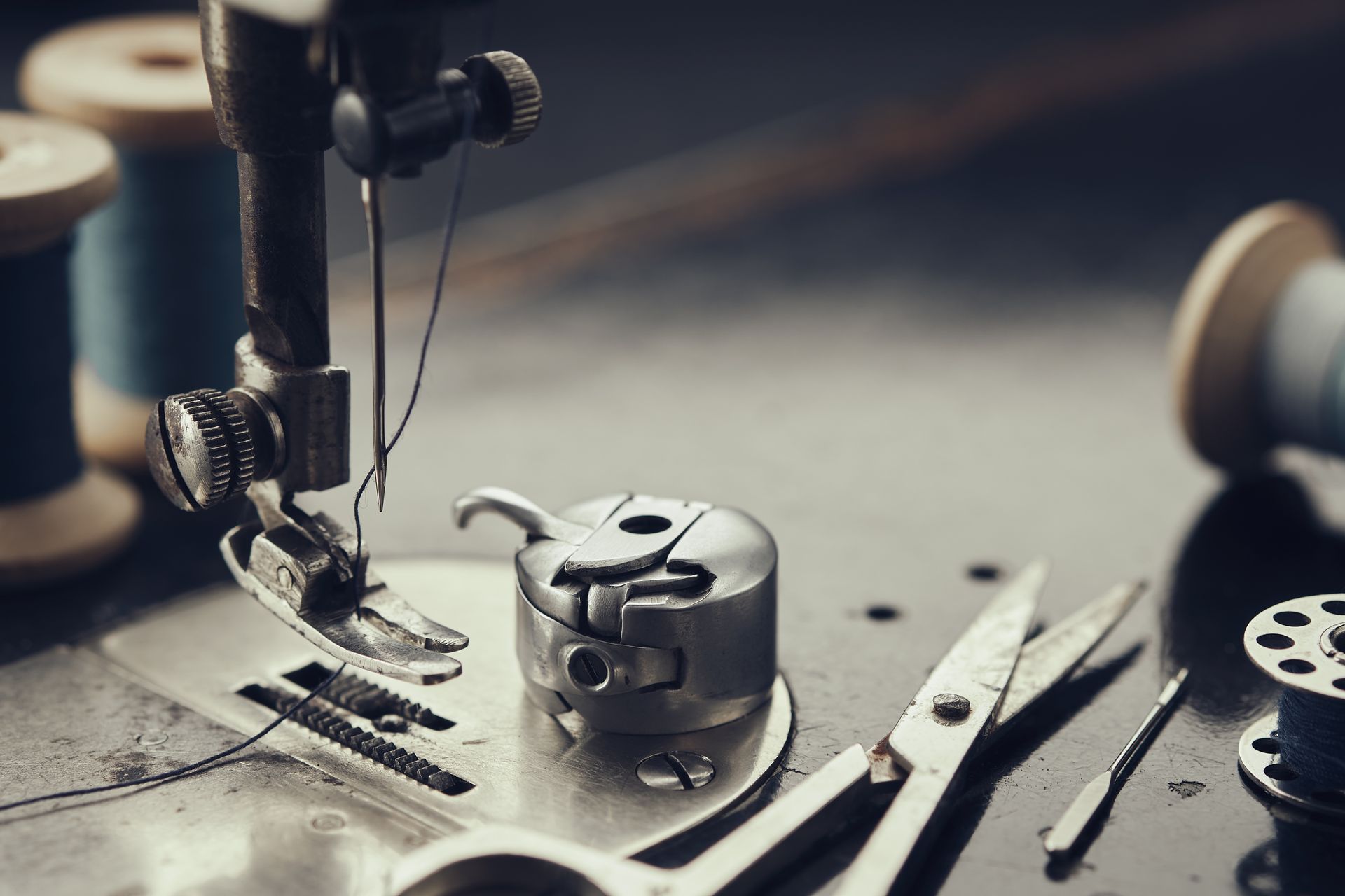 Gros plan sur le pied-de-biche, l'aiguille, le boîtier de canette et les ciseaux d'une machine à coudre posée sur une table de couture en métal.