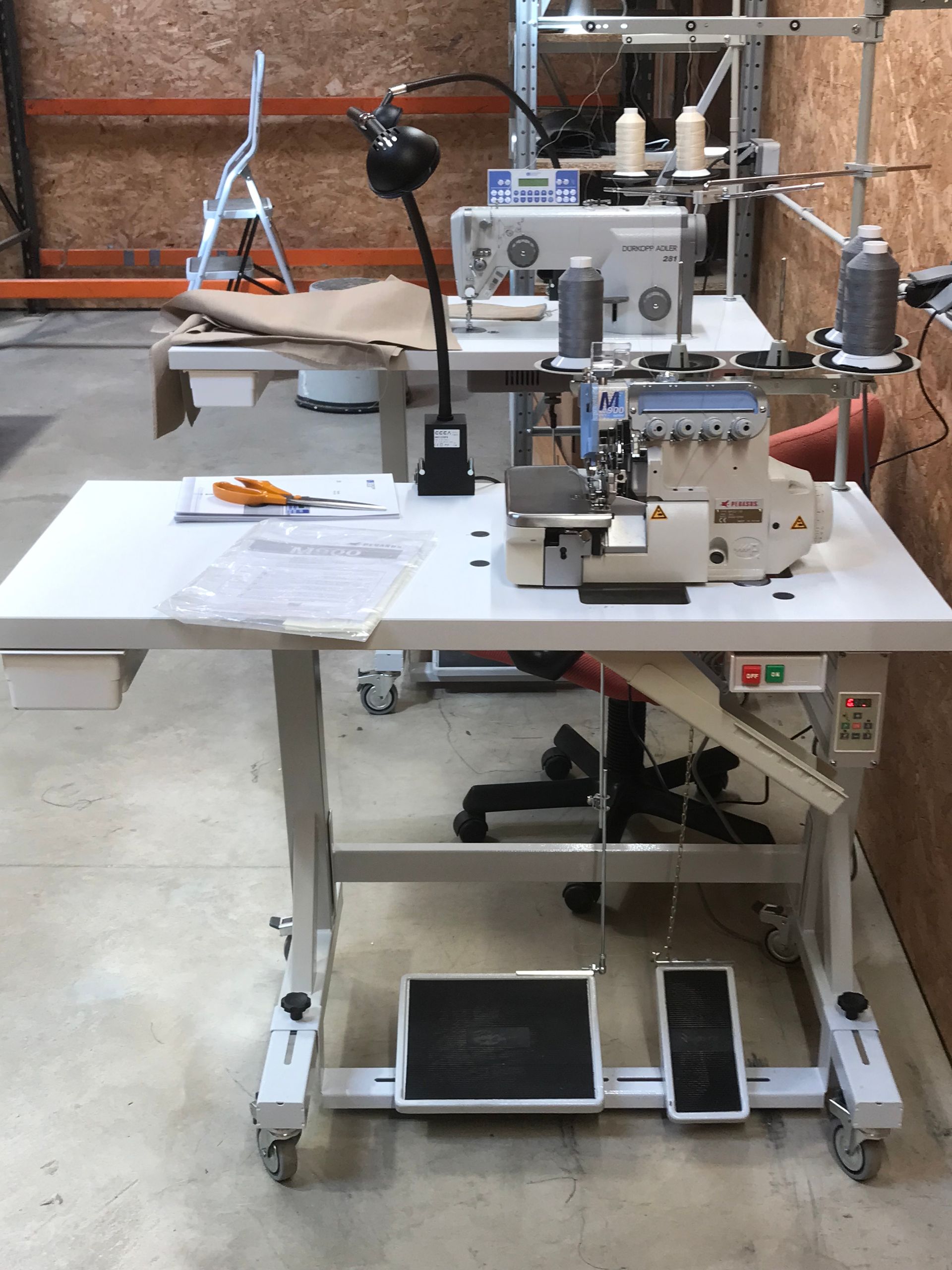 Machines à coudre industrielles avec pédales et lampes de travail sur des tables dans un atelier.