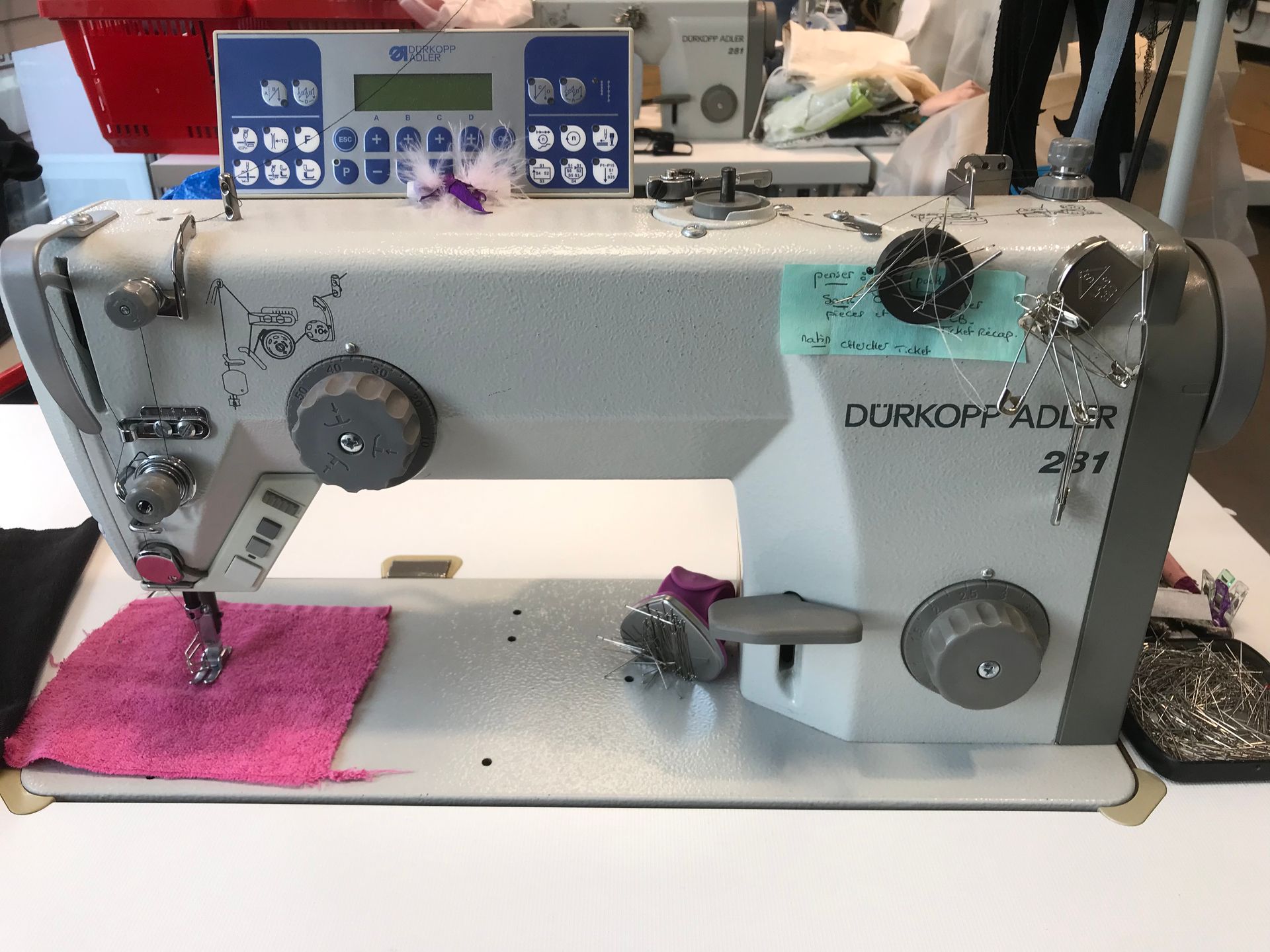 Une machine à coudre industrielle Dürkopp Adler 291 sur une table avec un morceau de tissu rose sous le pied presseur.