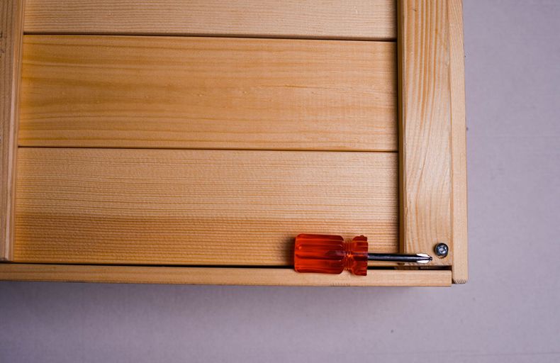 Gros plan sur le coin d’une armoire en bois, avec un tournevis rouge posé sur une vis métallique